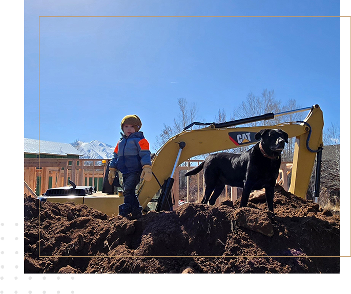 A dog and a man standing in front of a cat backhoe.